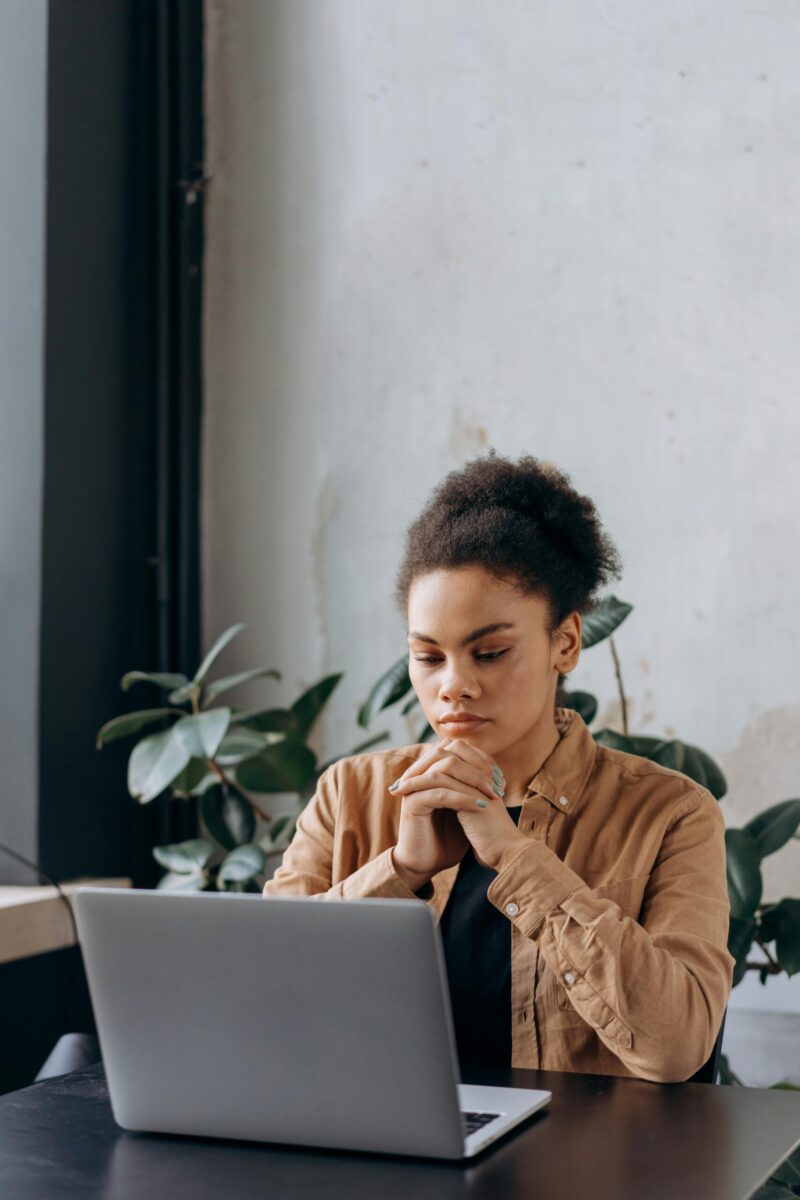 A young woman in casual attire works intently on a laptop in a cozy home office setting.
